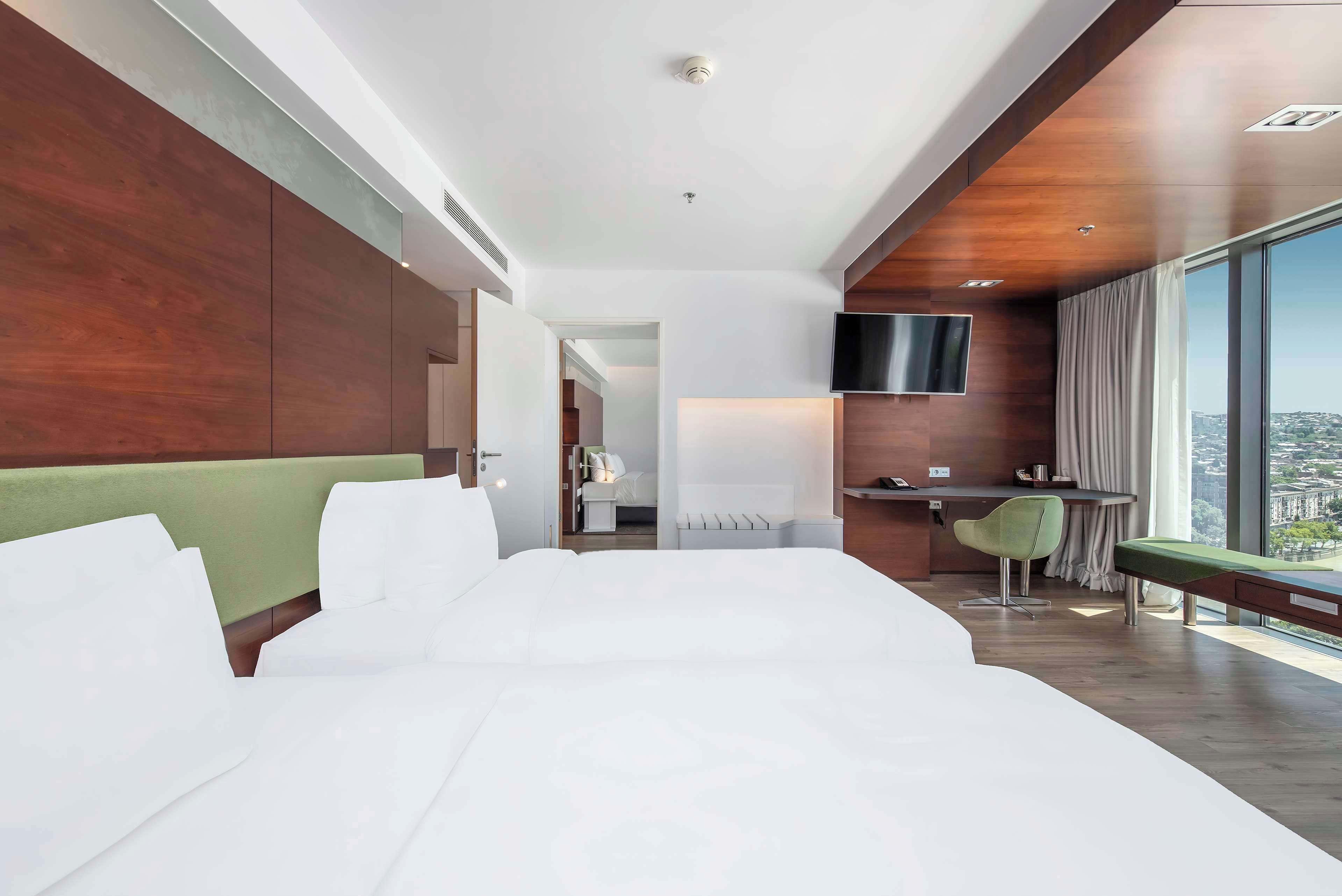 A modern hotel room with a large bed, a desk, a chair, and a TV.