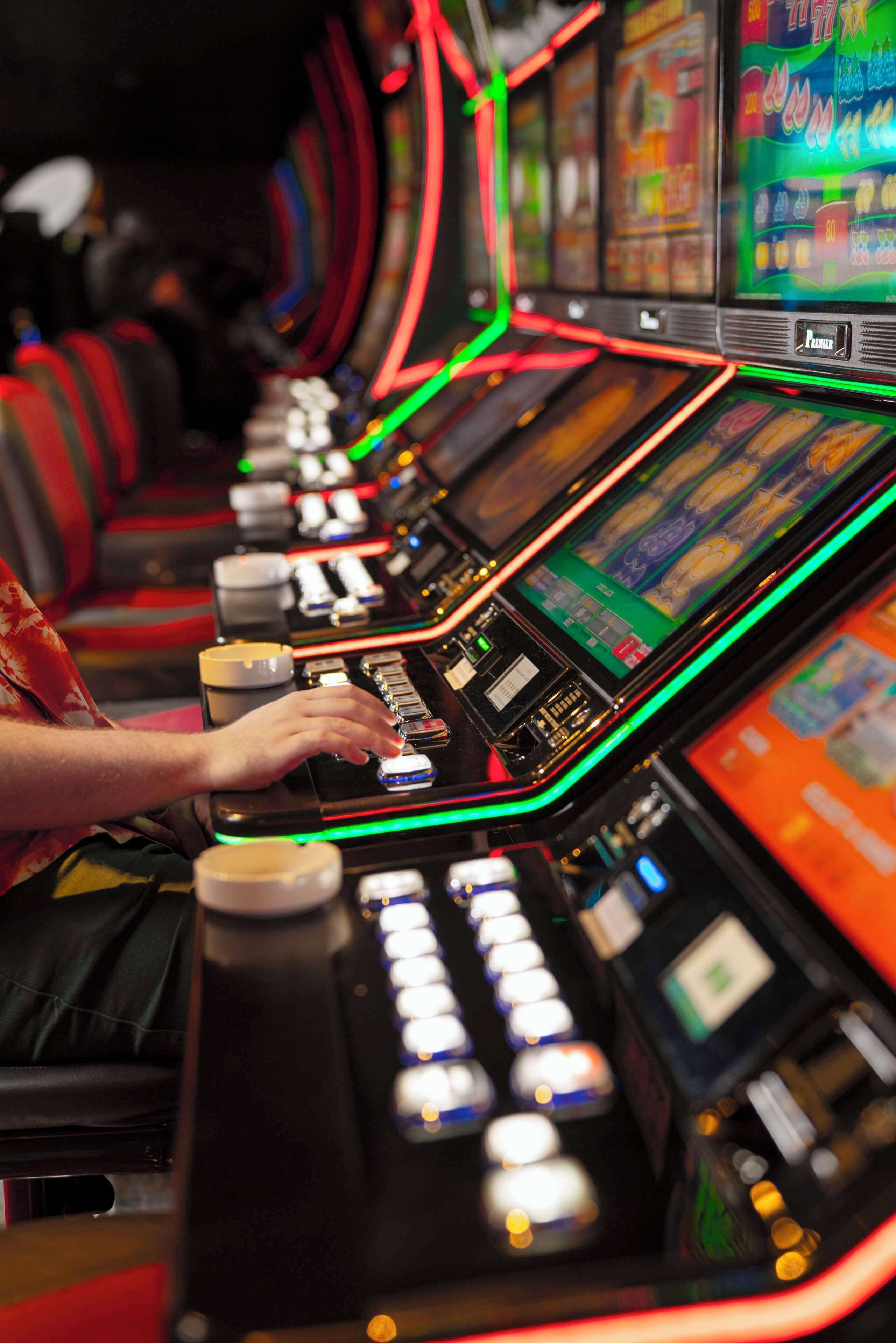 A row of slot machines with illuminated reels and a person operating one.