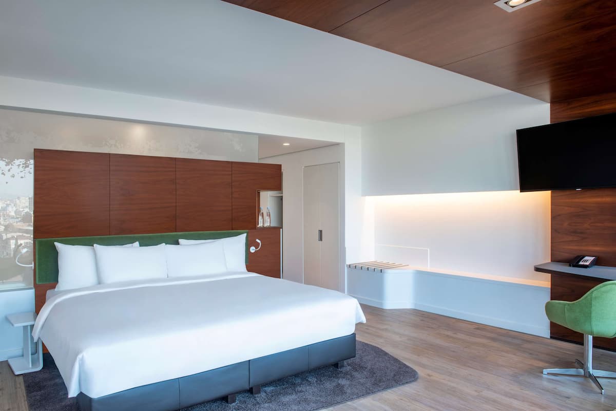 A modern hotel room with a large bed, a desk, and a television.