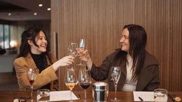 Two people toasting with wine glasses at a wooden table with a menu and a metal container.
