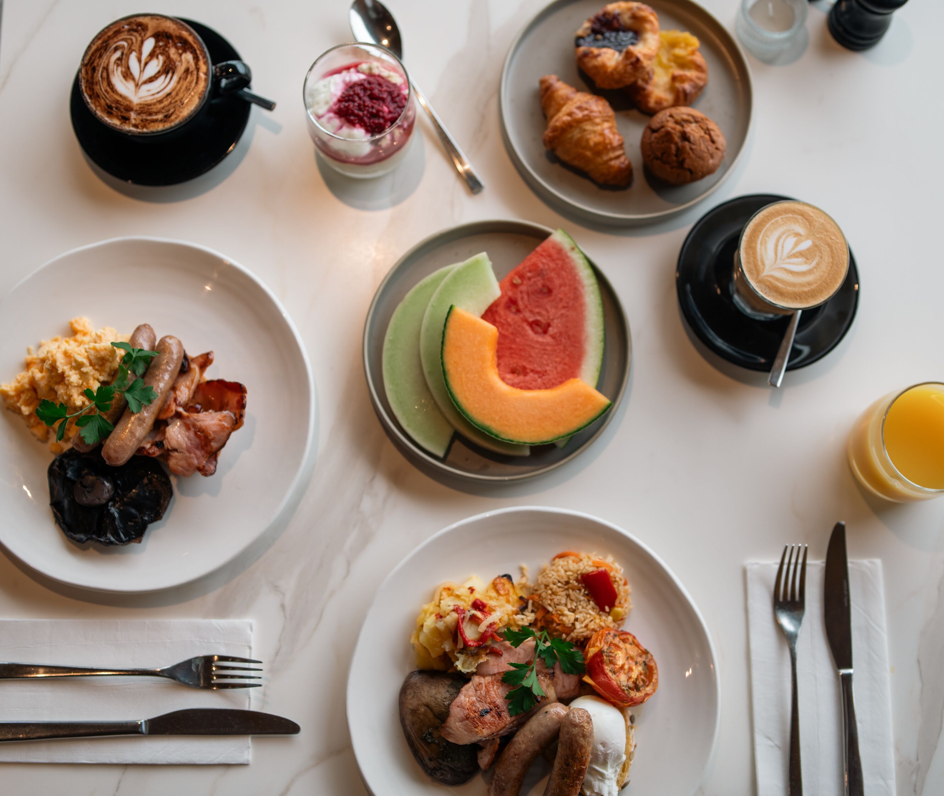 A breakfast setting with various dishes including eggs, sausages, and a watermelon slice.