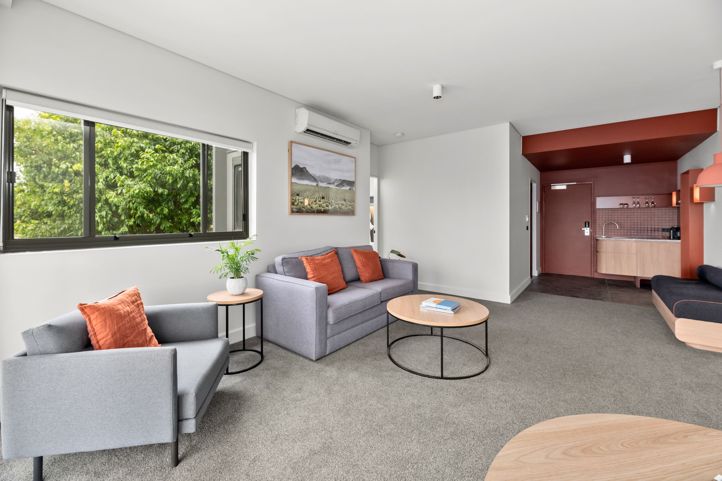 A modern living room with a grey sofa, a small round table, and a view of a kitchen area.