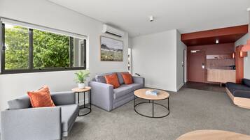A modern living room with a grey sofa, a small round table, and a view of a kitchen area.
