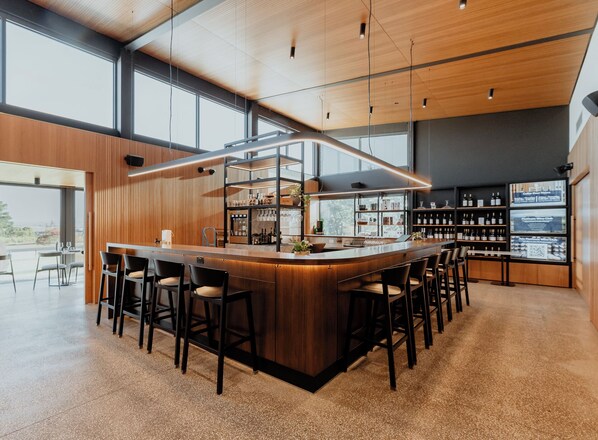 A modern bar area with a wooden bar counter, seating, and wine shelves. - Balgownie Estate Yarra Valley (Yarra Glen)