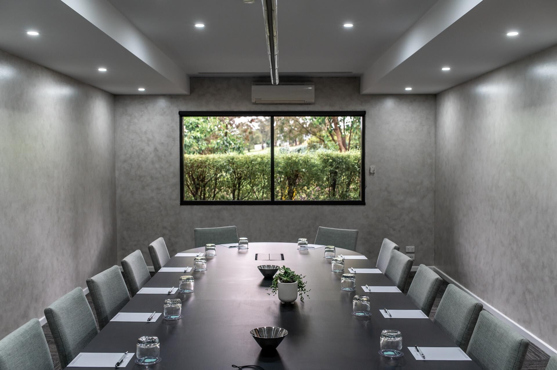 A conference room with a long table, chairs, a projector, and a large window with a view of greenery.