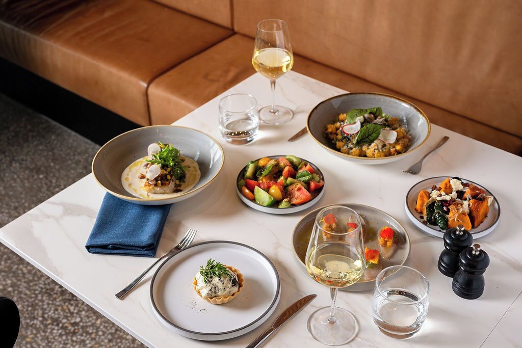 A dining table with various dishes and glasses of white wine, set on a marble surface with a blue napkin and salt and pepper shakers.