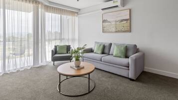 A modern living room with a grey sofa, a round coffee table, and a large window with sheer curtains.