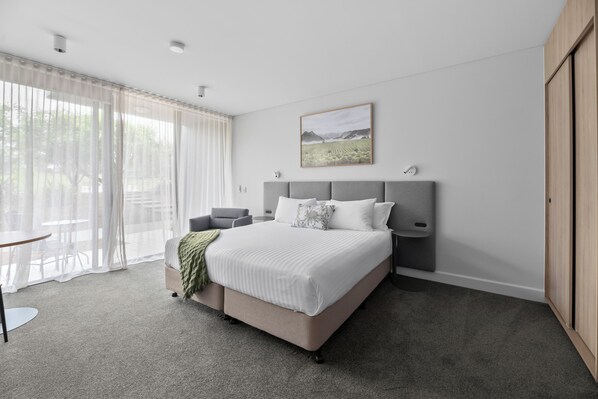 A modern bedroom with a large bed, a bedside table, a chair, and a window with sheer curtains. - Balgownie Estate Yarra Valley (Yarra Glen)