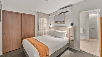 A modern bedroom with a large bed, a wooden wardrobe, an air conditioning unit, a framed picture on the wall, and a shower area.