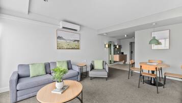 Una sala de estar moderna con un sofá gris, una mesa de centro redonda y una zona de comedor con mesa y sillas de madera.