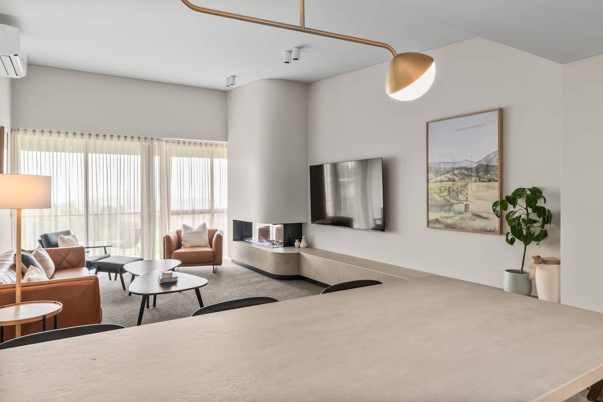 A modern living room with a large flat-screen TV, a sofa, a coffee table, and a dining area.