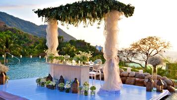 An outdoor wedding setup with a white canopy, floral arrangements, and a poolside table.
