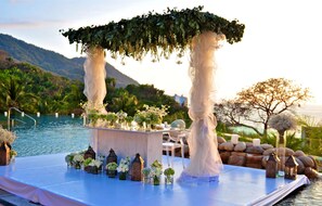 An outdoor wedding setup with a white canopy, floral arrangements, and a poolside table.