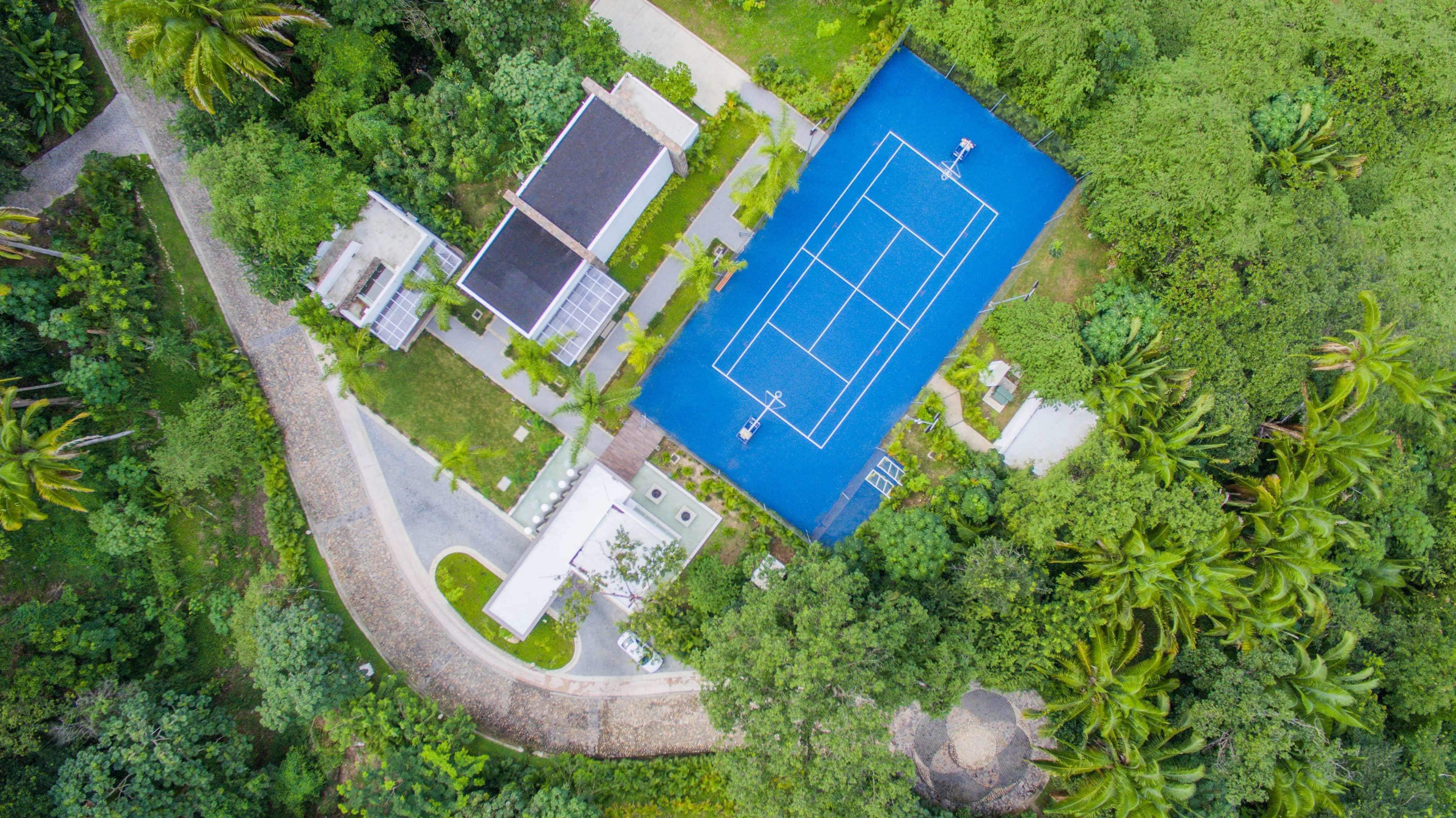 Vista aérea de una zona residencial con cancha de tenis, piscina y abundante vegetación.