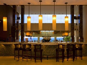 A bar area with a marble countertop, multiple bar stools, and hanging pendant lights.