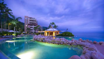 Piscina de un resort con jardín de rocas, palmeras y un edificio con balcones.