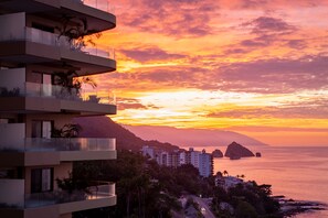 A multi-story building with balconies, a coastal view, and a sunset.