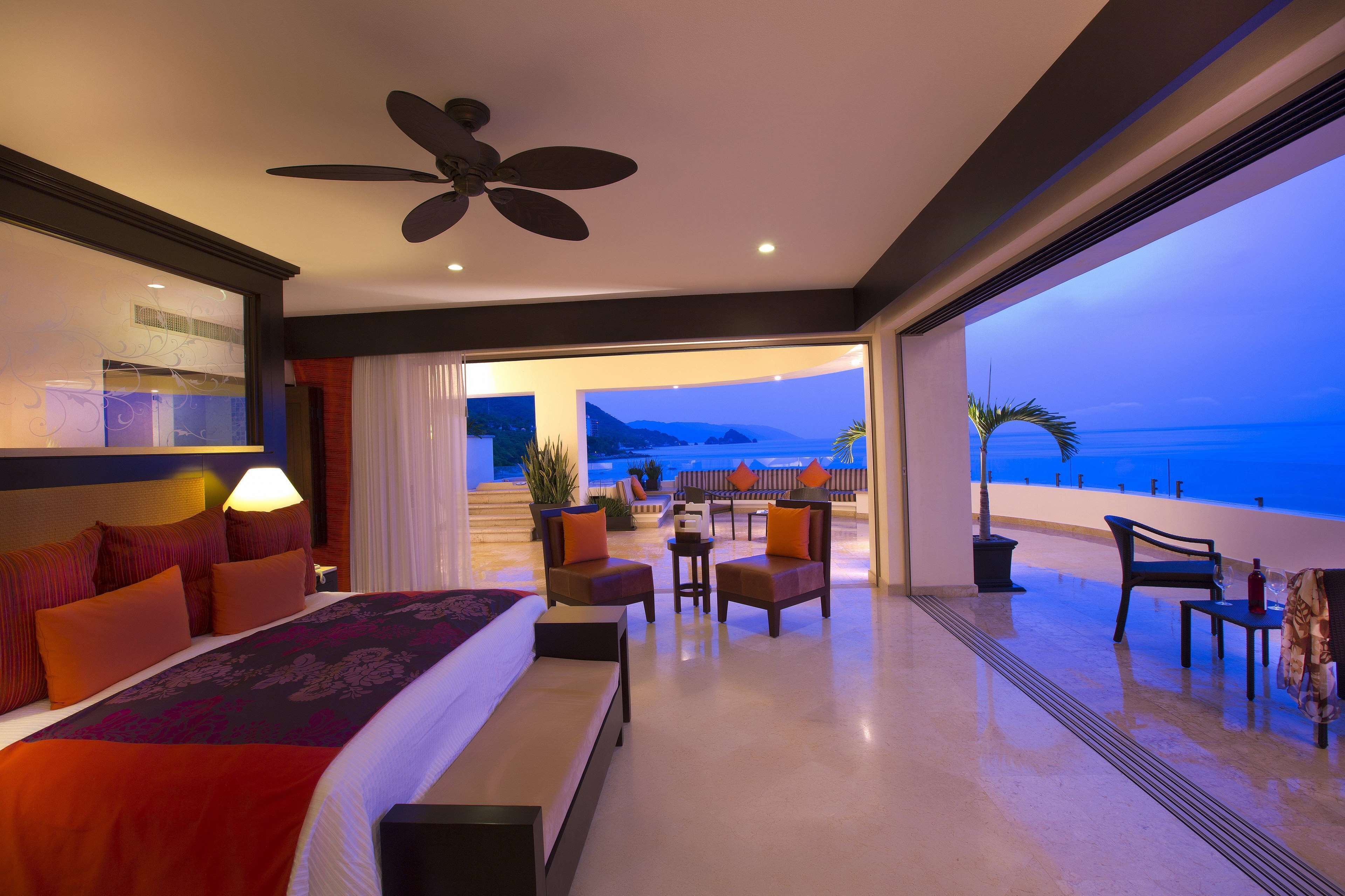 Una habitación de hotel moderna con una cama grande, un ventilador de techo y un balcón con vistas al océano.