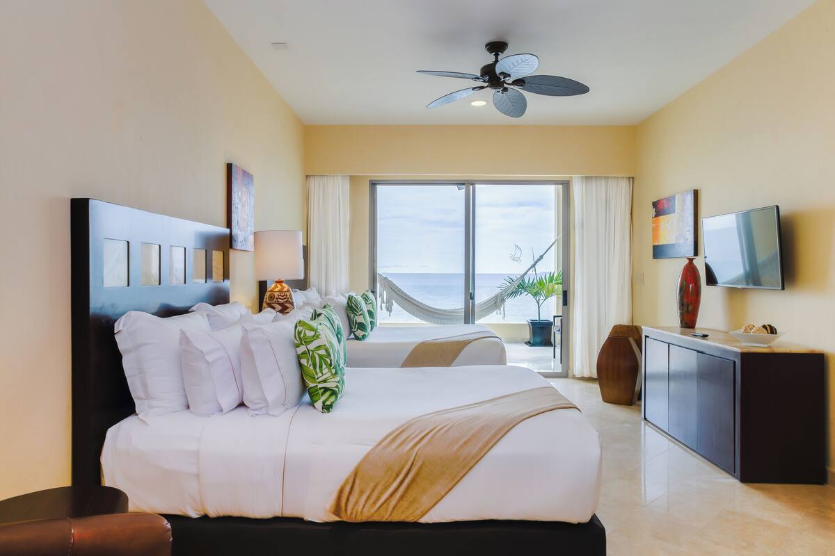 Een hotelkamer met een groot bed, een plafondventilator, een televisie en uitzicht op de oceaan.