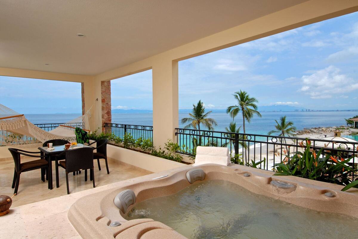 Een balkon met een jacuzzi, eettafel, stoelen en uitzicht op het strand en de oceaan.