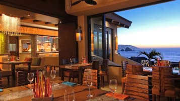 Un restaurante con mobiliario de madera, vistas al océano y una zona de bar con candelabro.