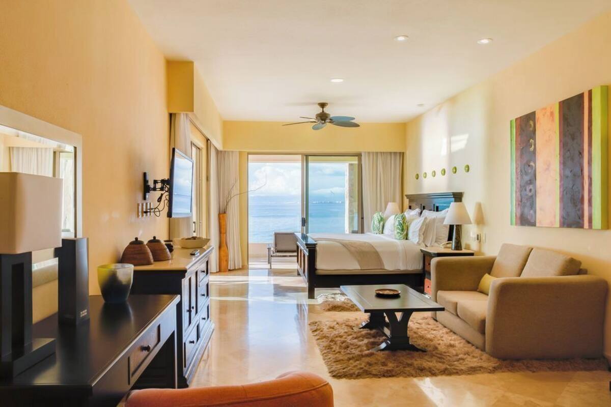 Een hotelkamer met een bed, een bureau, een bank, een televisie en uitzicht op de oceaan.