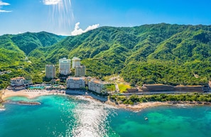 A coastal resort with multiple high-rise buildings, a beach, and lush green hills.