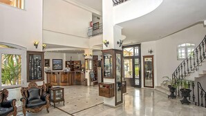 Eine geräumige Lobby mit hoher Decke, einer imposanten Treppe und einem Empfangstresen.