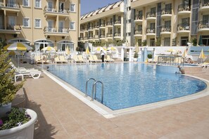A pool area with lounge chairs and umbrellas, surrounded by a multi-story building with balconies.