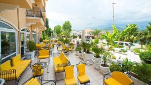 Eine Terrasse mit gelben Stühlen und Tischen, umgeben von Topfpflanzen und Blick auf die Stadt.