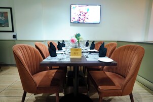 A dining table with numbered place settings, orange upholstered chairs, and a television mounted on the wall.