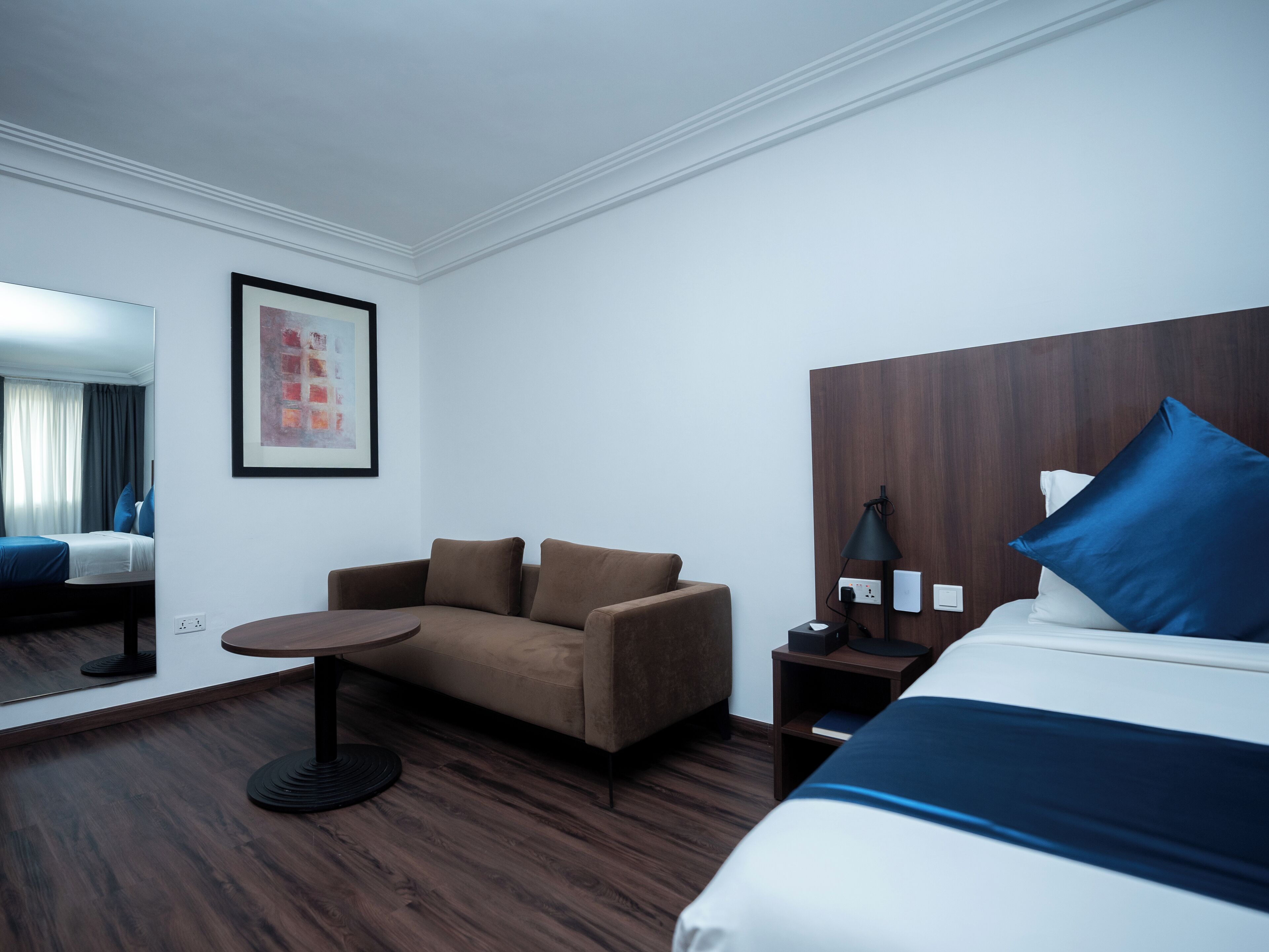 A hotel room with a bed, a sofa, a small table, a lamp, and a nightstand.