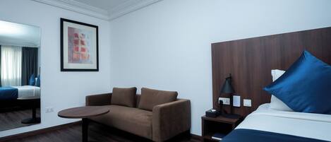 A hotel room with a bed, a sofa, a small table, a lamp, and a nightstand.