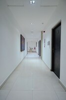 A long, narrow hallway with white walls, a tiled floor, and doors on one side.