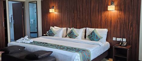Quarto de hotel com uma cama grande, duas mesas de cabeceira, um pequeno sofá e um tapete estampado.