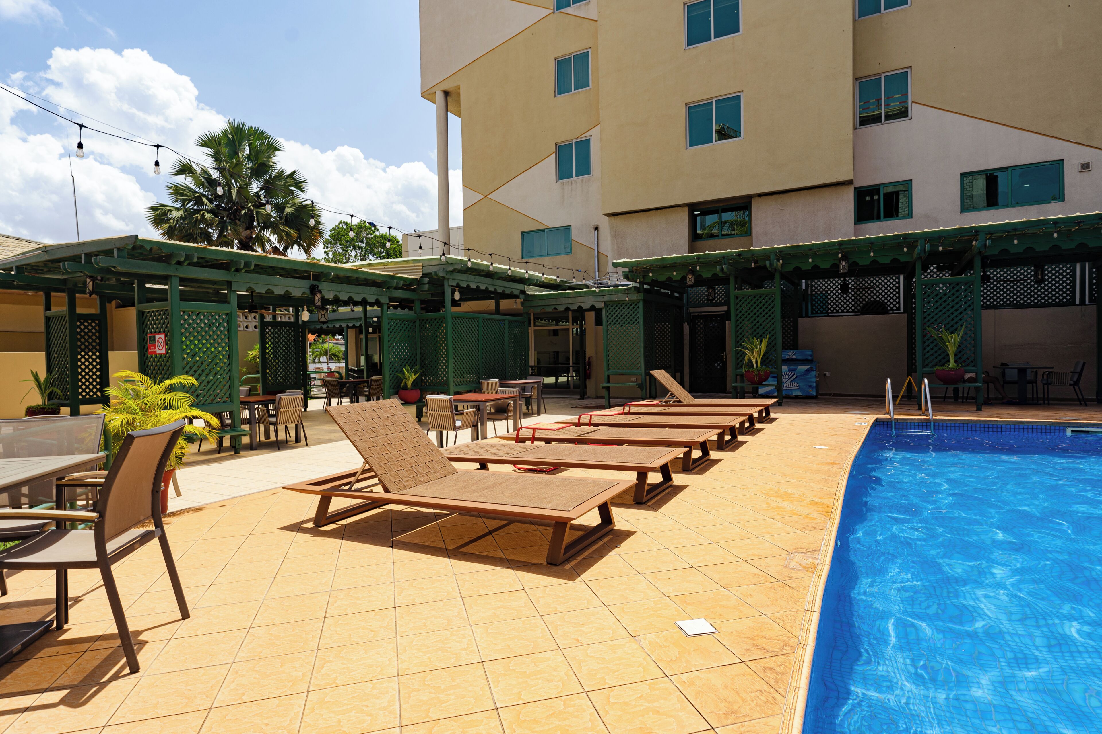 Zona de piscina de hotel con tumbonas, piscina y mobiliario exterior.