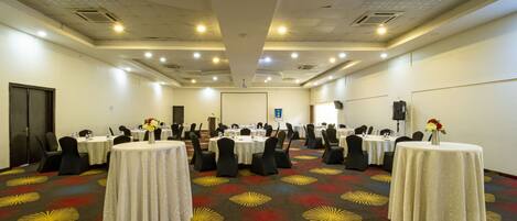 Una sala de conferencias con varias mesas y sillas, equipada con micrófonos y botellas de agua.