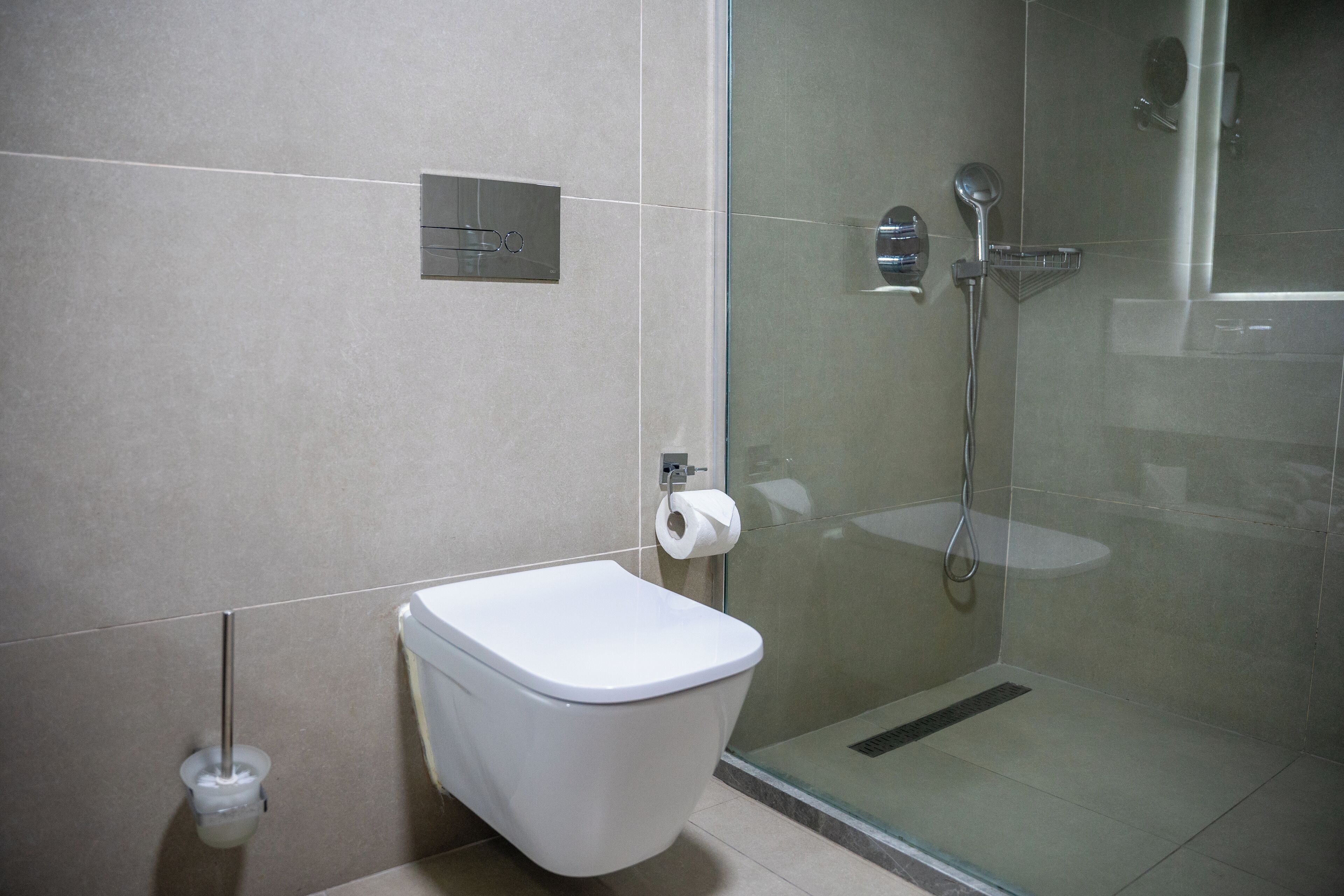 Een moderne badkamer met een toilet, een douchecabine van glas en een toiletrolhouder aan de muur.
