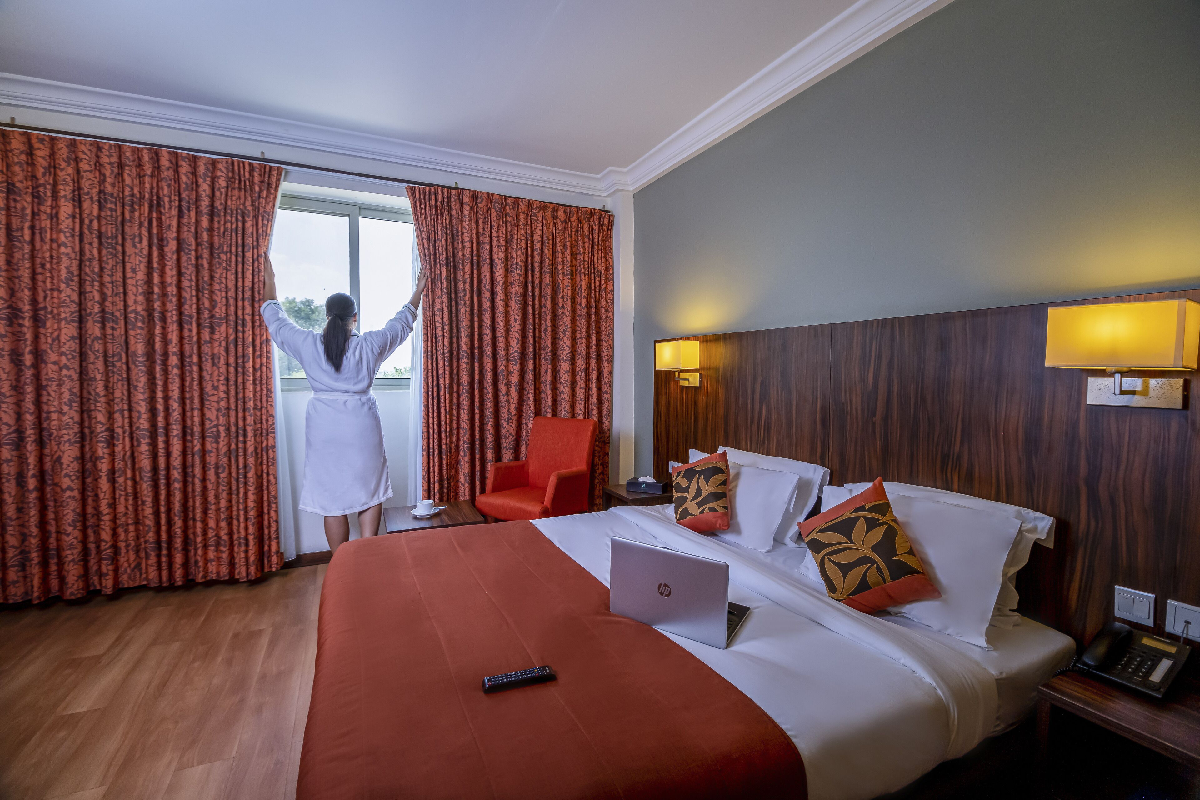 Ein Hotelzimmer mit einem Bett, einem Laptop, einer Fernbedienung und einem Sessel.