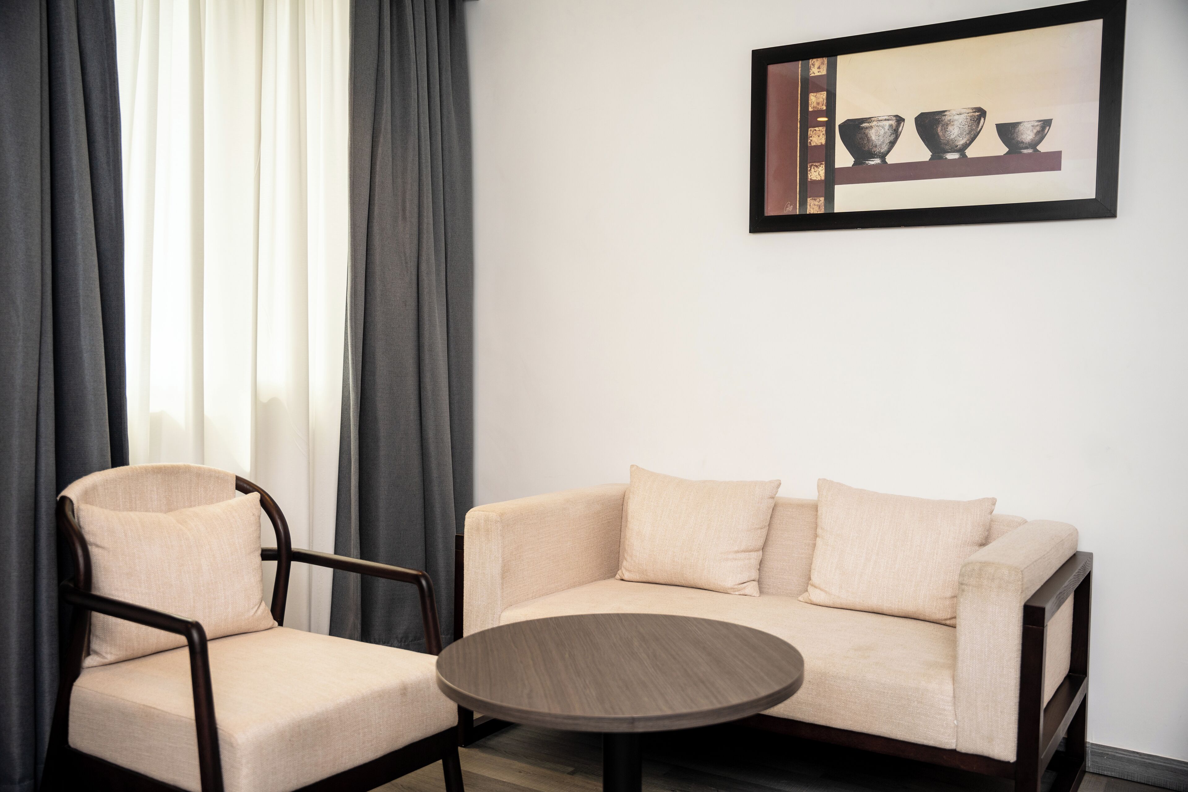 Ett modernt rum med en beige soffa, ett träbord och en mörk fåtölj. En inramad tavla hänger på väggen.