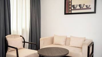 A modern room with a beige sofa, a wooden coffee table, and a dark armchair. A framed picture hangs on the wall.