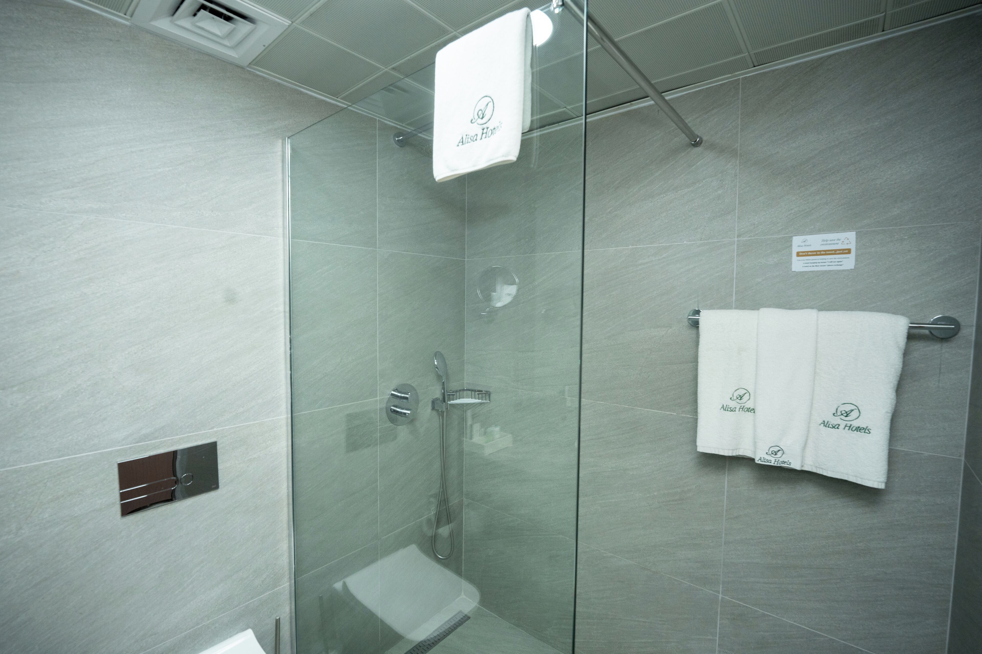 Un área de ducha moderna con separador de vidrio, cabezal de ducha de mano y toallero con toallas.