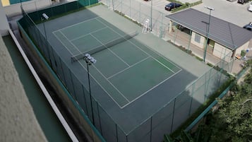 Un court de tennis en plein air, doté d’un filet et entouré d’une clôture verte.