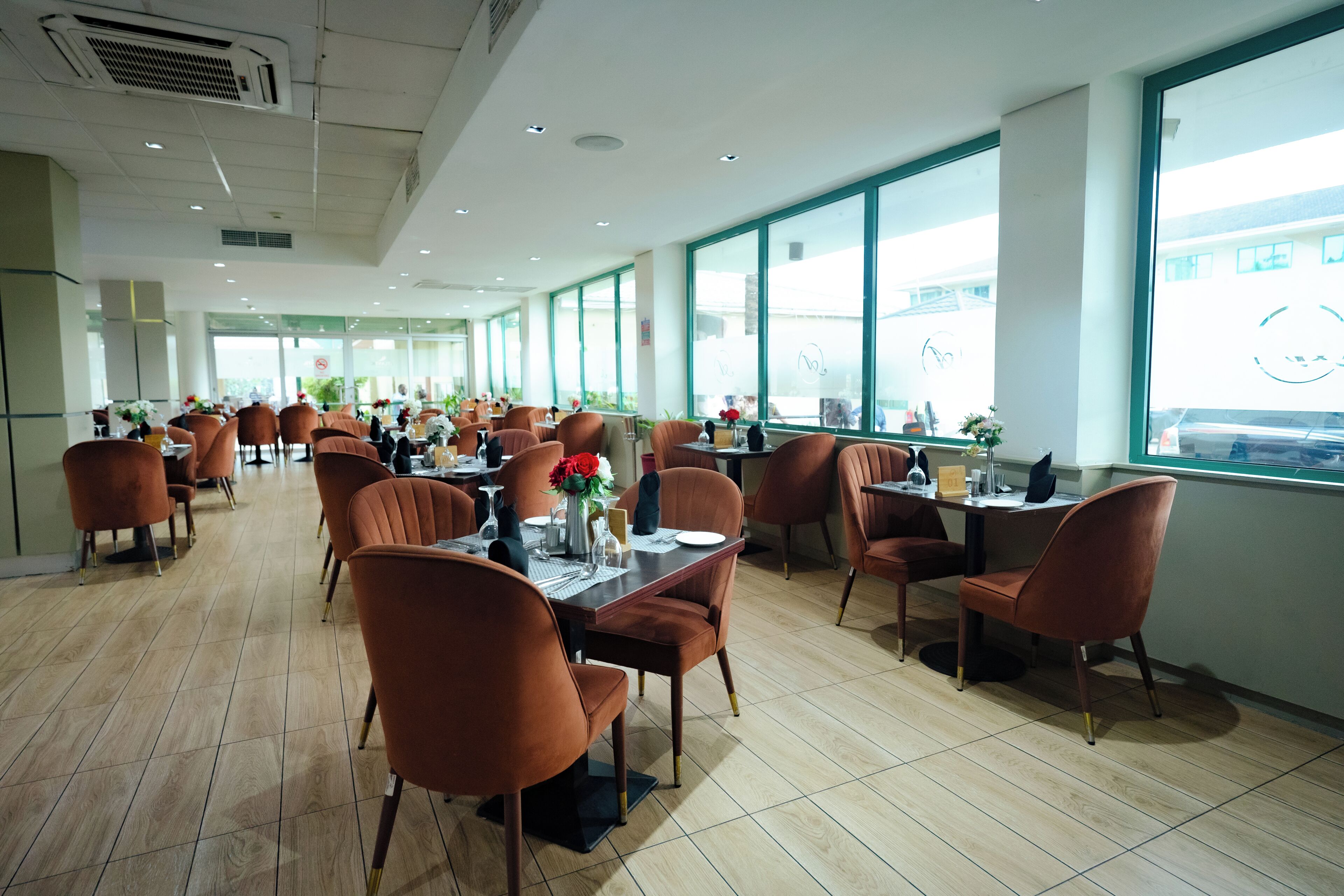 A spacious dining area with multiple tables and chairs, large windows, and a tiled floor.