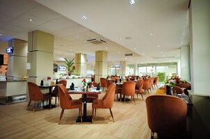 Un ristorante spazioso con soffitti alti, illuminazione moderna e diverse disposizioni di posti a sedere.