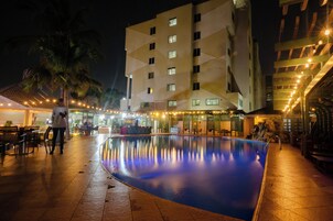 A swimming pool with a tiled deck, a palm tree, and a building with multiple windows and balconies.
