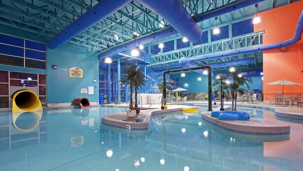 Une piscine intérieure aux couleurs bleu et orange, avec un toboggan et des palmiers.