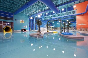 An indoor swimming pool with a blue and orange color scheme, a slide, and palm trees. - Garner Hotel Gillette South by IHG (Gillette)