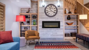 Un salon moderne avec une grande horloge, une cheminée, un canapé, une table basse et un tapis à motifs.