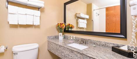 A bathroom with a toilet, sink, and mirror. There are towels hanging on a rack and a bouquet of flowers on the sink.